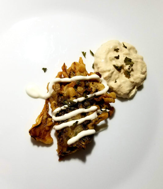 Hen of the Woods fritters with chipotle ranch drizzle and ramp leaf gremolata on a white plate