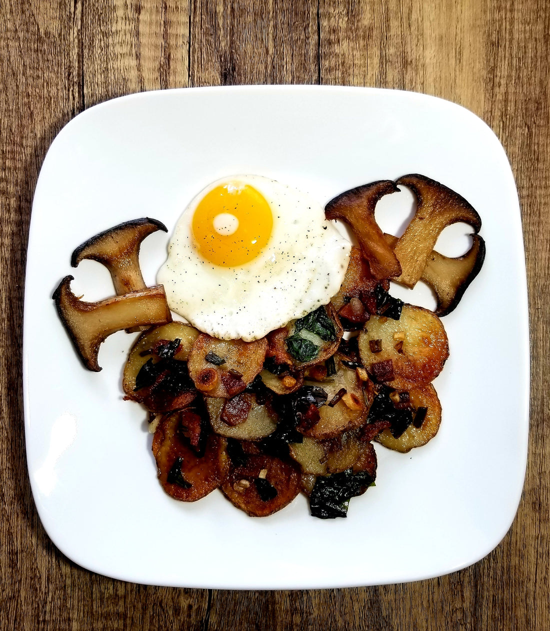 Ramp and potato hash with King Trumpet mushrooms and sunny side up egg on a white plate