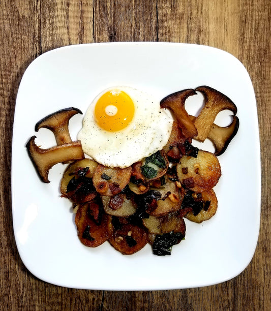 Ramp and potato hash with King Trumpet mushrooms and sunny side up egg on a white plate