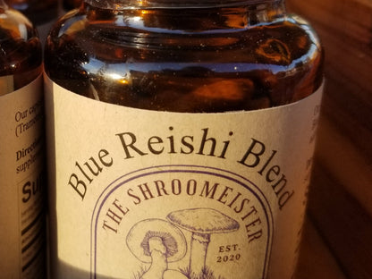 Close up view of a glass bottle containing capsules labeled Blue Reishi Blend Mushroom Supplements with a white cap.