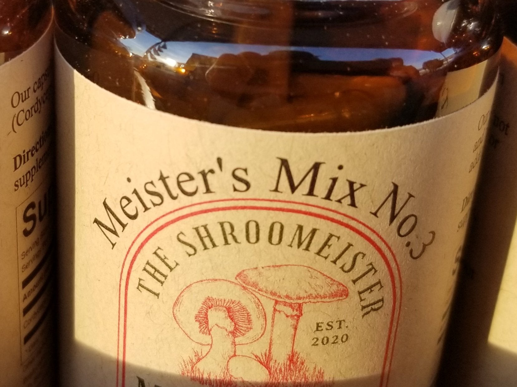 Close up view of A glass bottle containing capsules labeled Meister's Mix No.3 Mushrooms with a white cap.